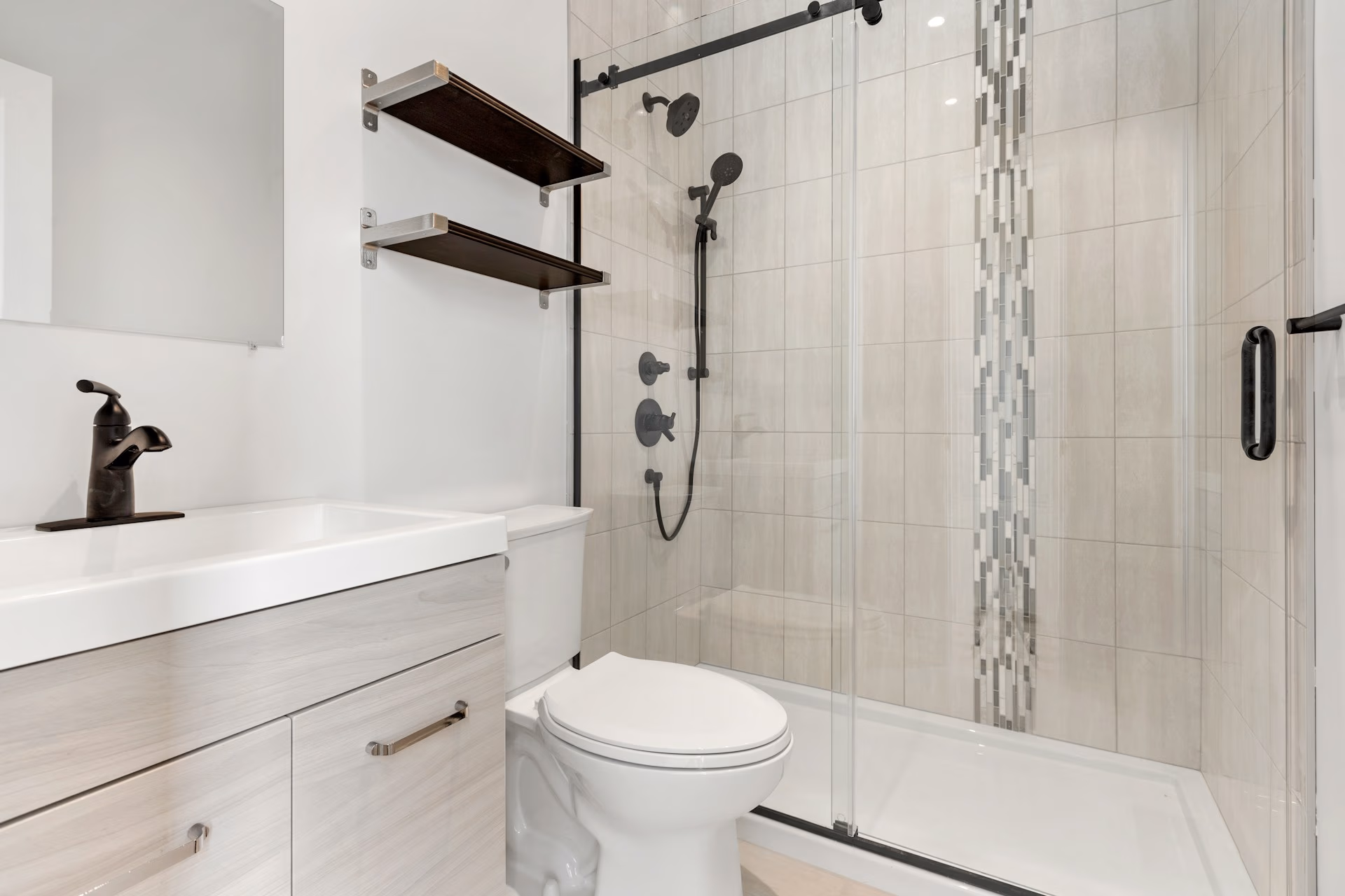Modern bathroom with a glass shower, white toilet, light wood vanity, and black fixtures.