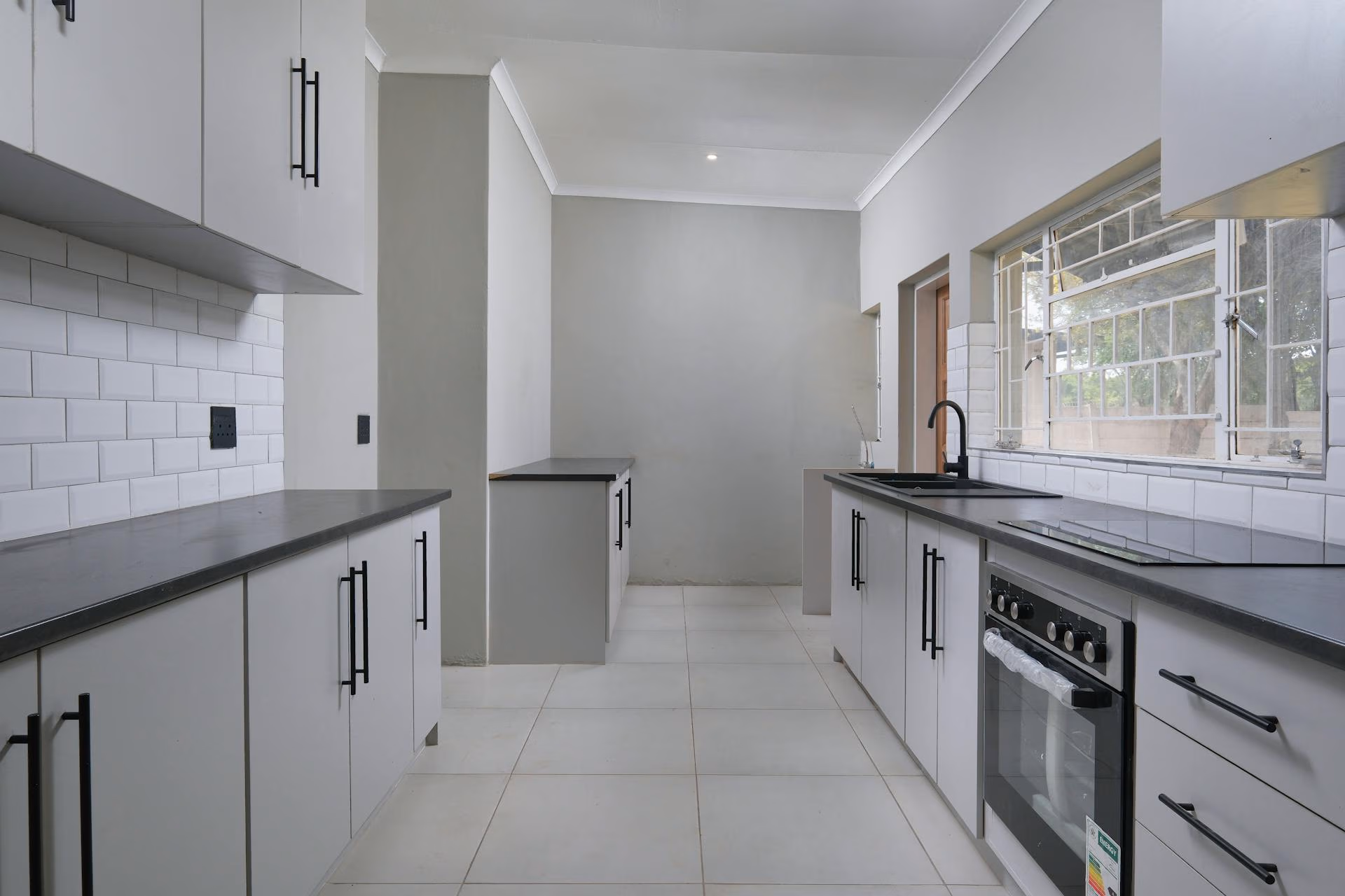 Modern kitchen with white cabinets, black hardware, black countertop, oven, and large window with bars.
