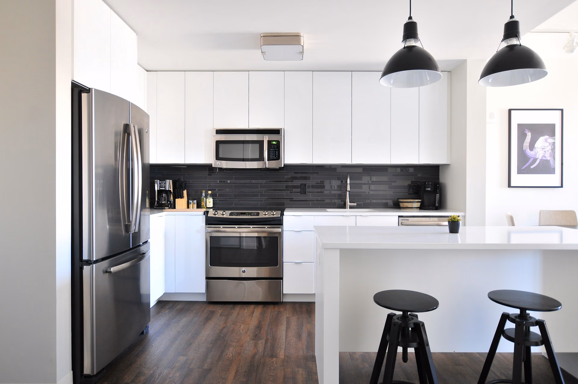 Modern kitchen with white cabinets, stainless steel appliances, black tile backsplash, and a white island with stools.