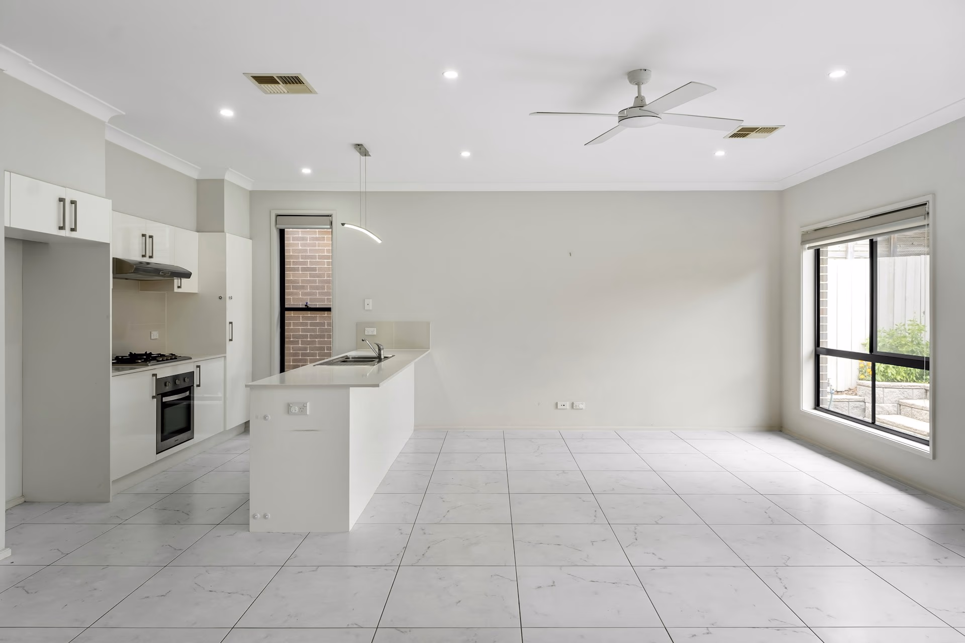 Empty modern kitchen and dining room with white cabinets, tiled floor, ceiling fan, and large window.