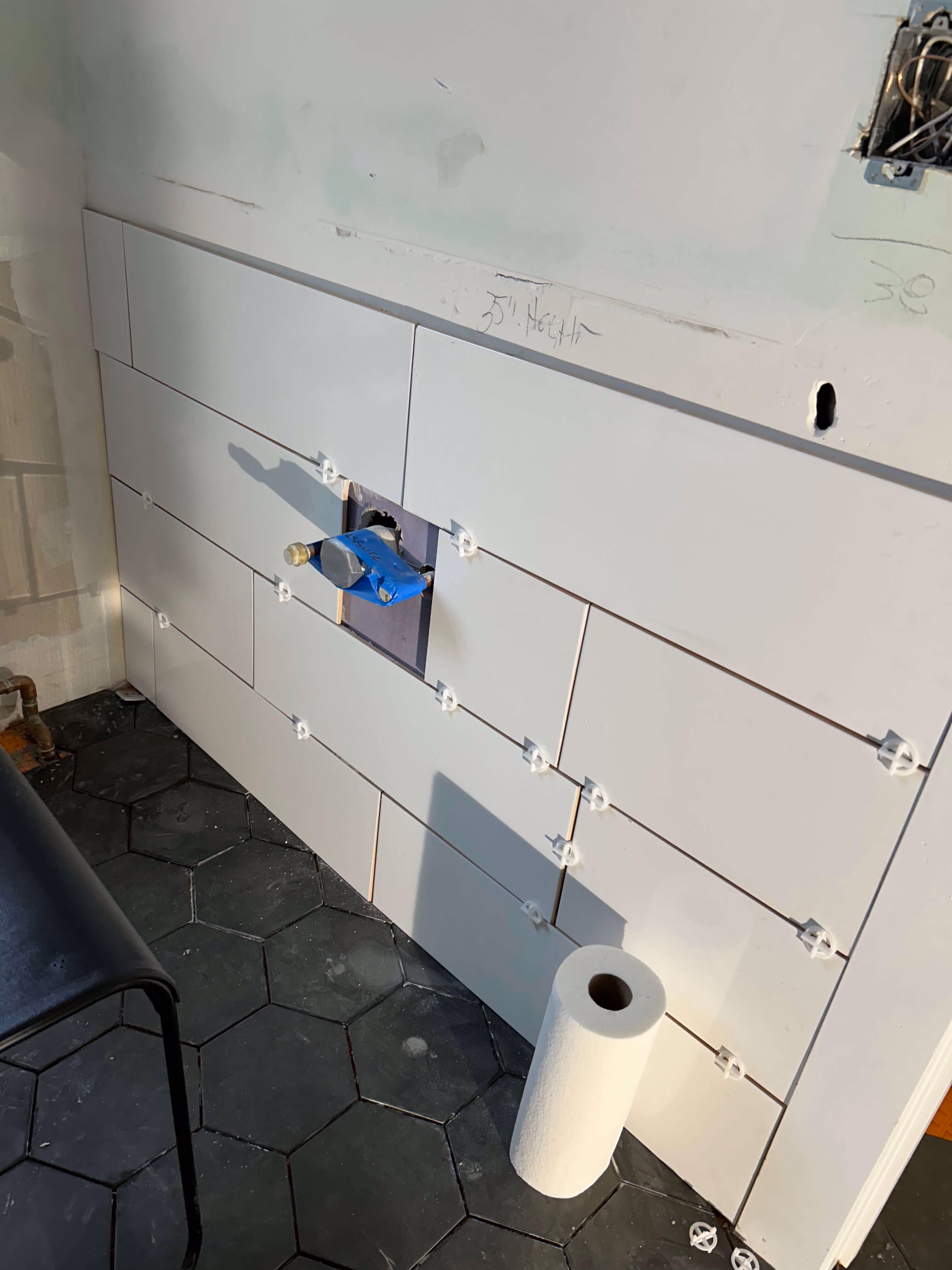 Partial wall tiling with rectangular white tiles in staggered layout and black hexagonal floor tiles.