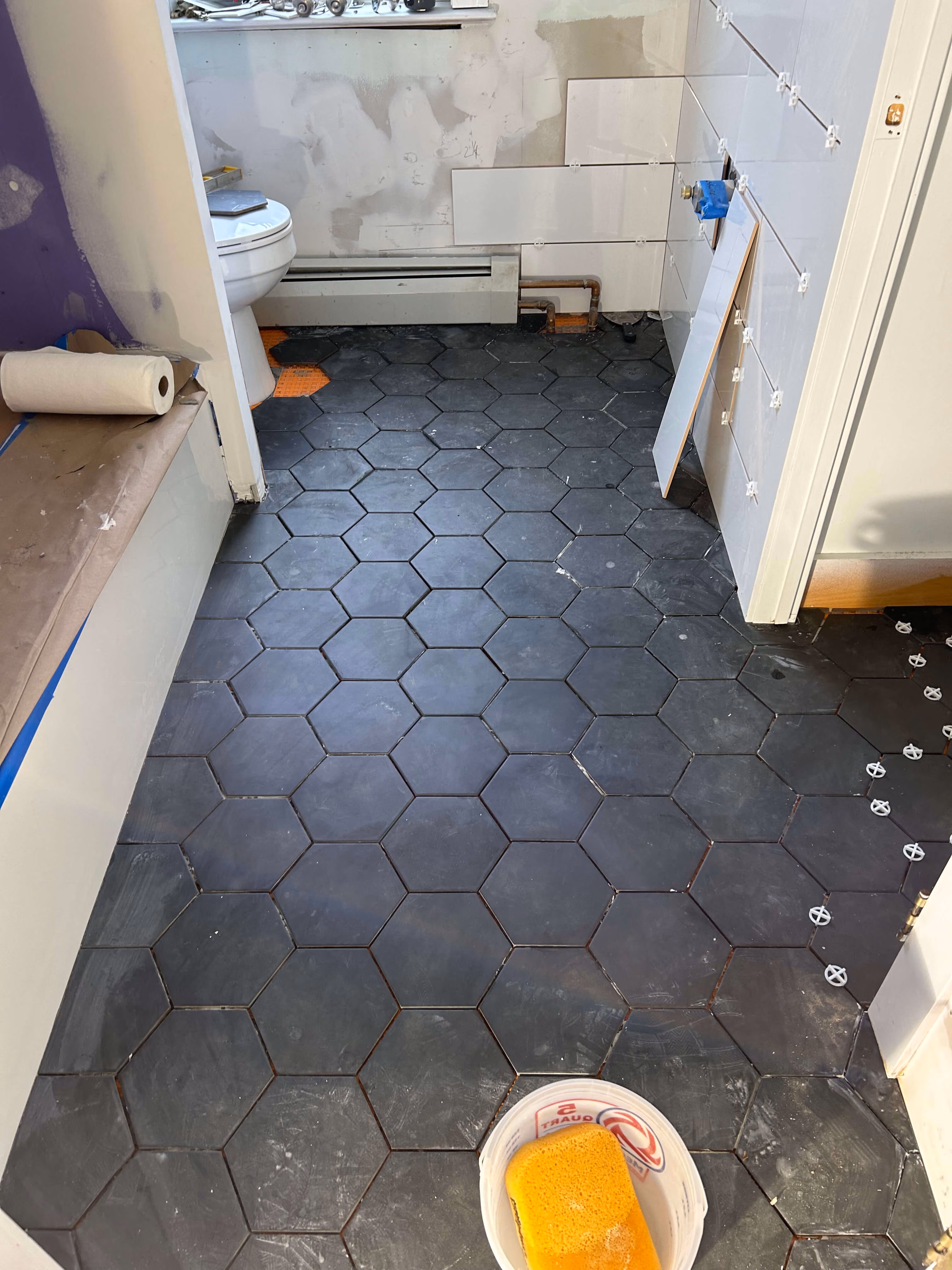 Bathroom renovation with black hexagon floor tiles partially installed and a toilet in the background.