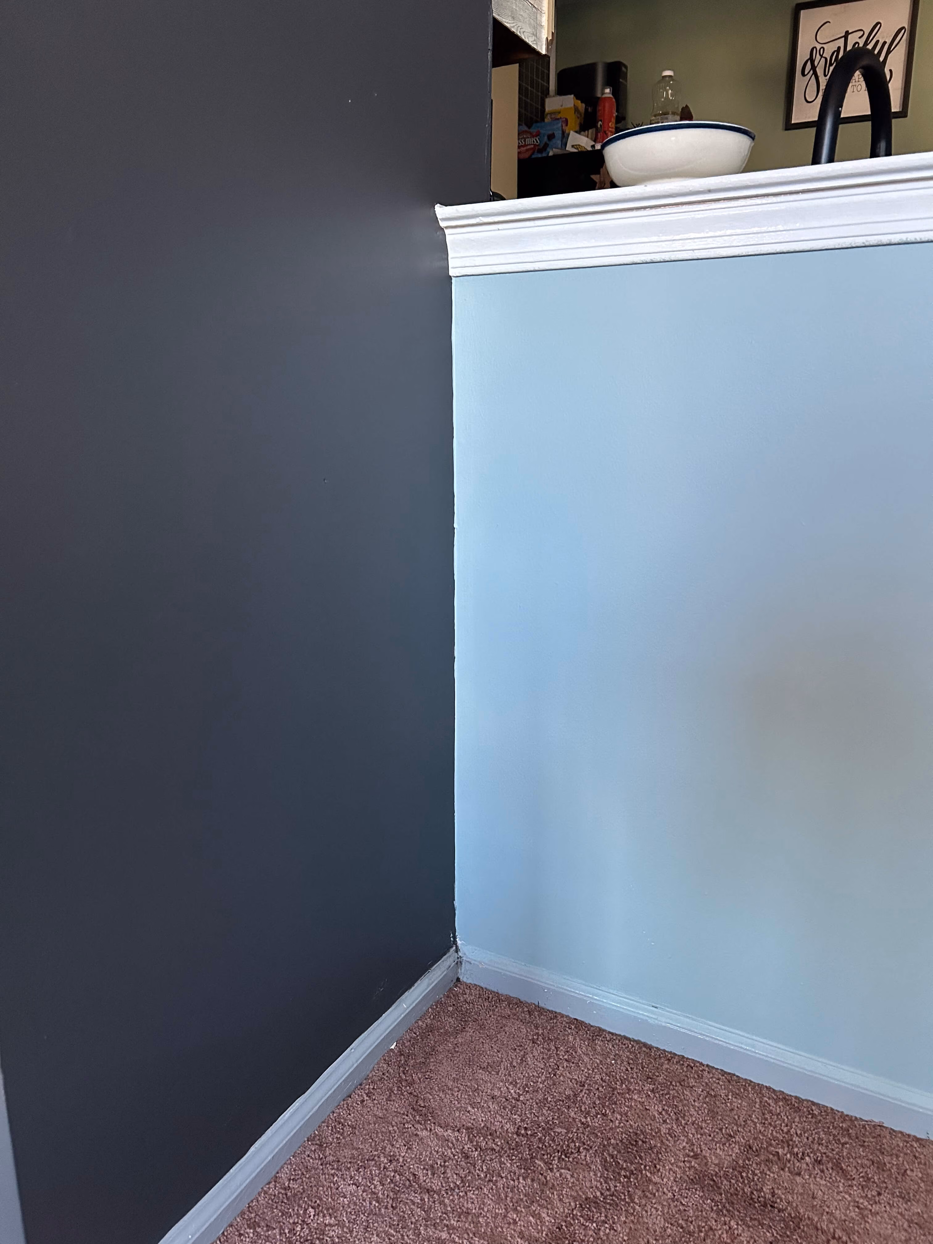 Corner of a room with dark gray and light blue walls, white trim, and brown carpet.