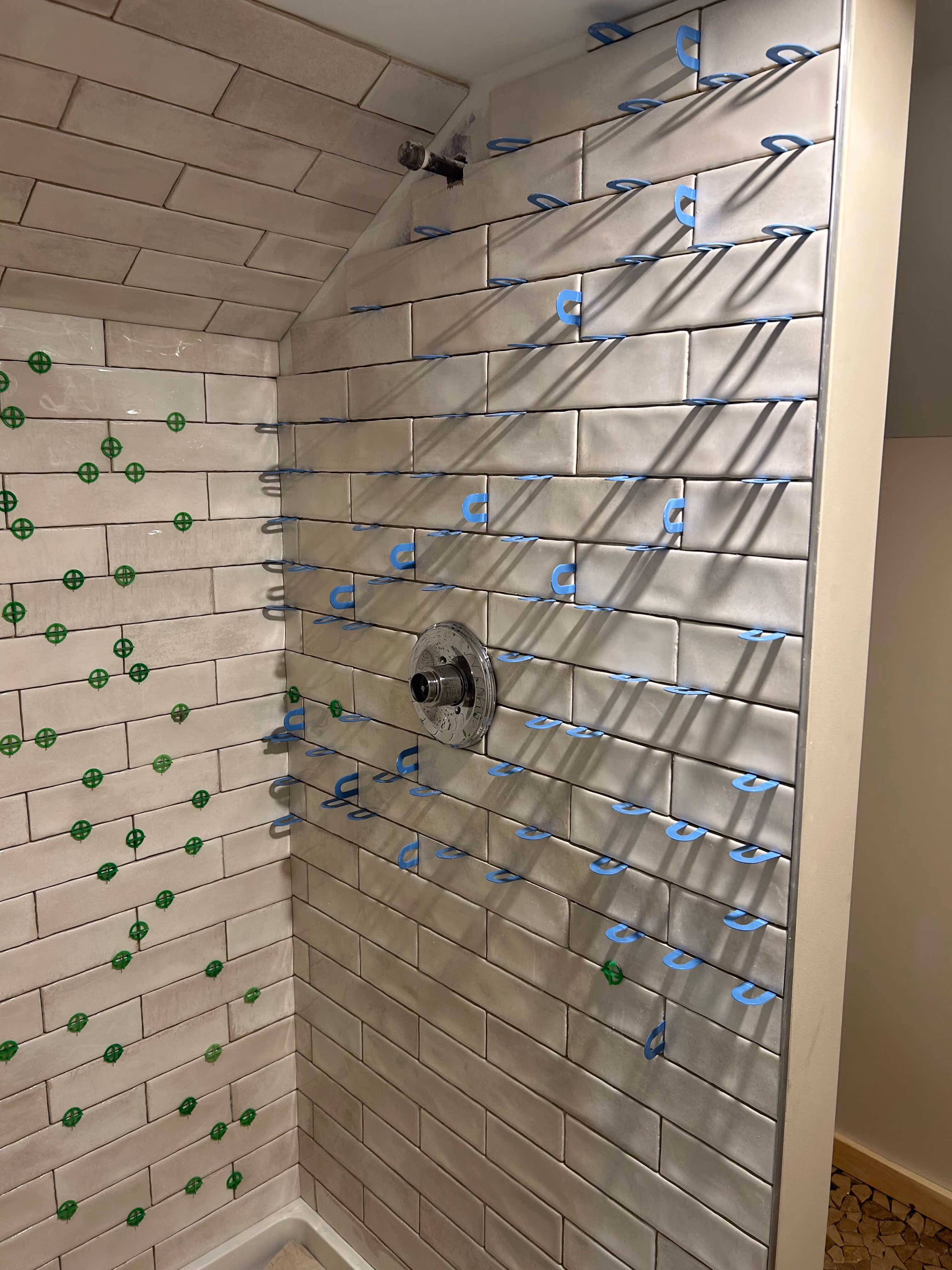 Partially tiled shower walls with white subway tiles and blue and green tile spacers in place.