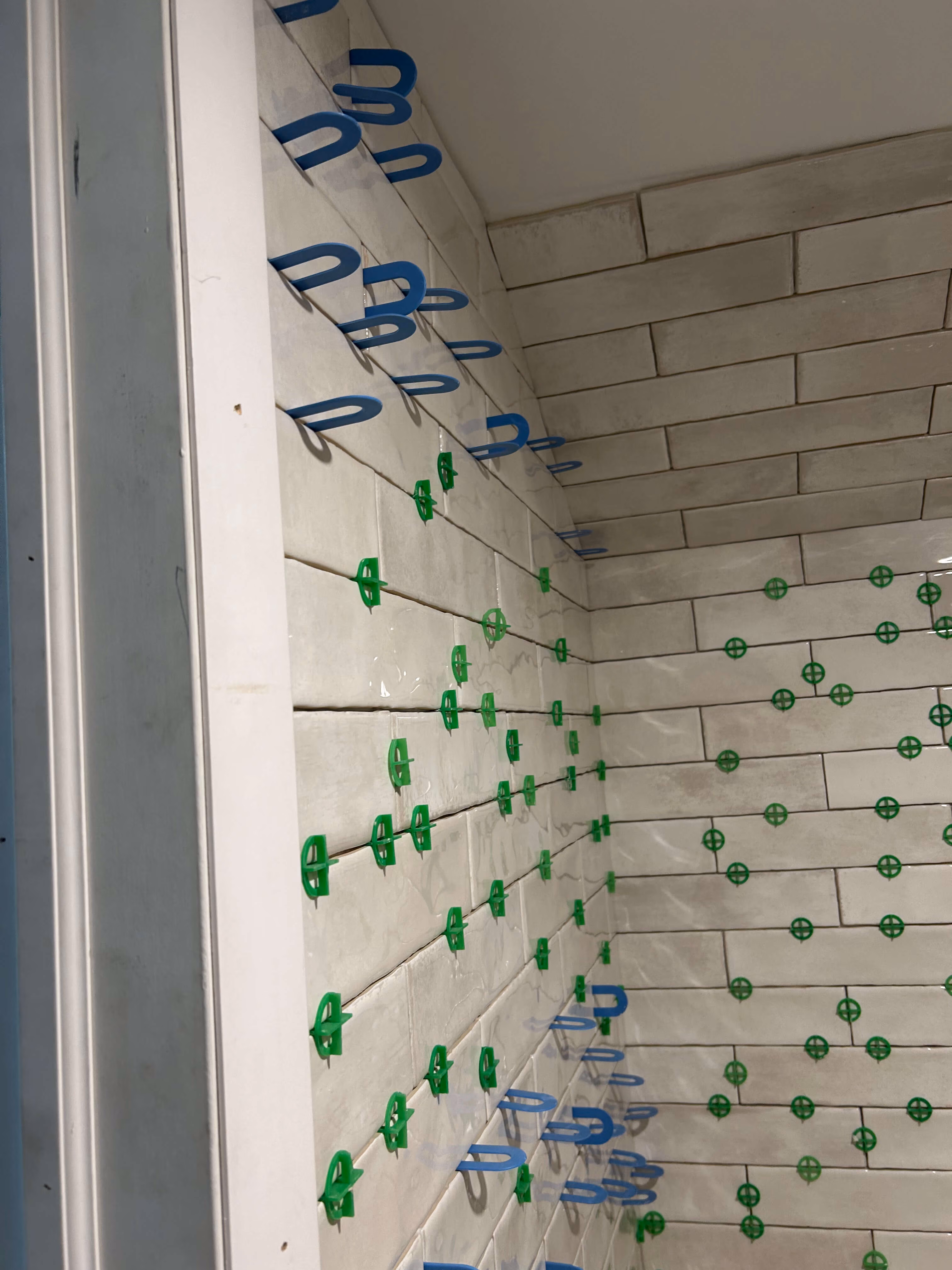 Light gray subway tiles on bathroom walls with green and blue tile spacers for grout alignment.