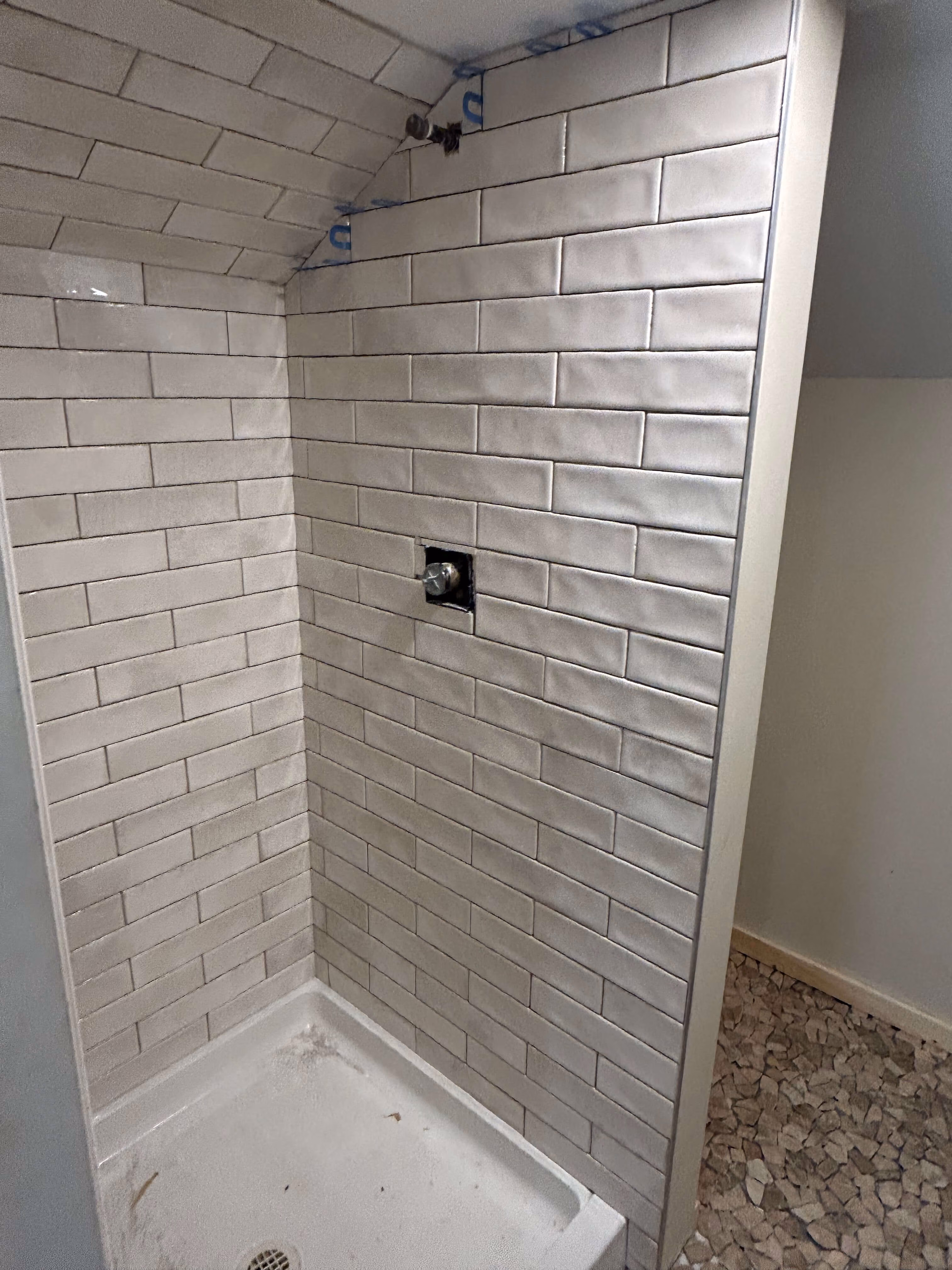 Corner shower area with white subway tiles and a small drain on the shower floor.