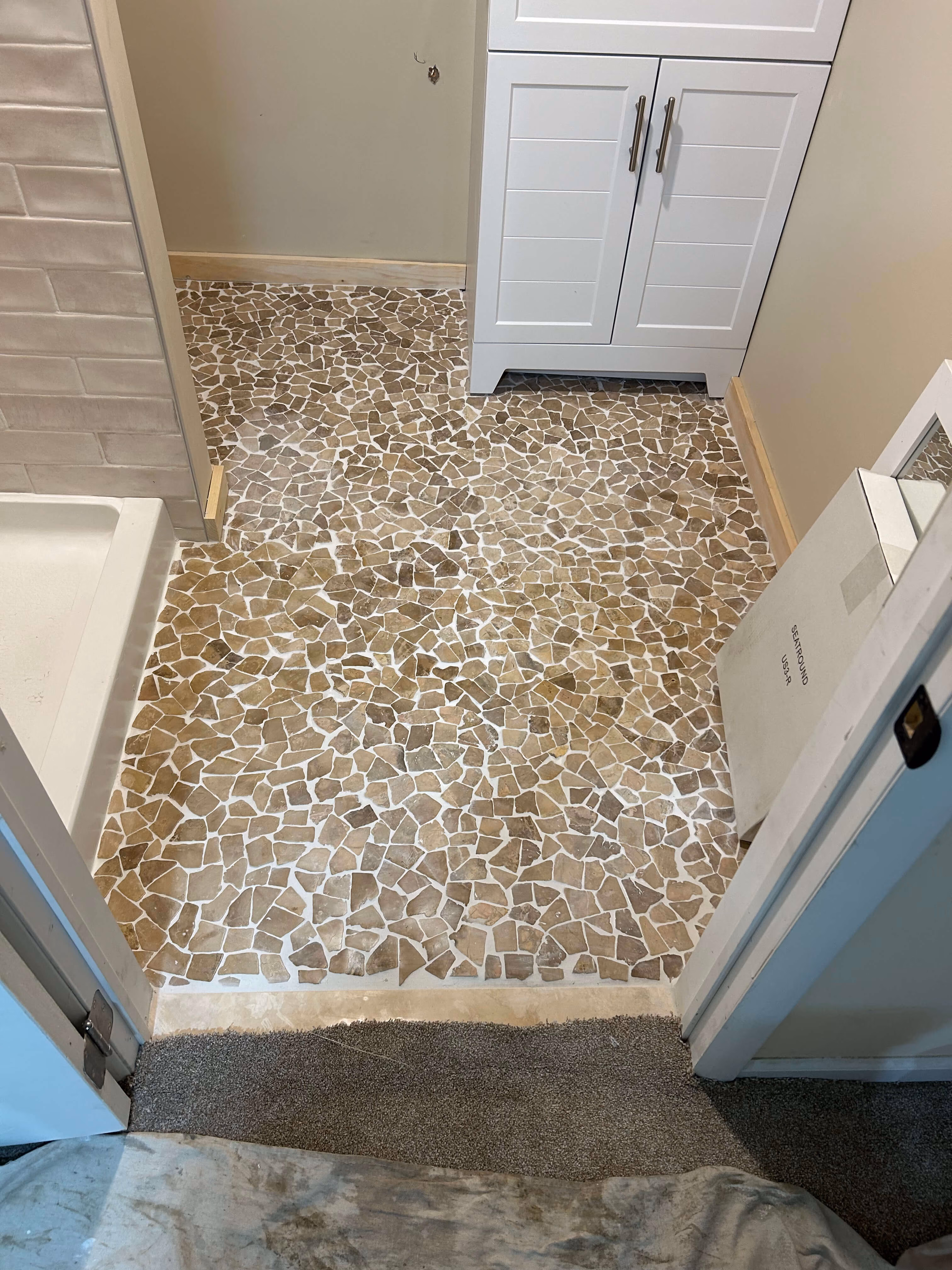 Small bathroom with irregular stone tile floor, white cabinet, beige walls, and carpeted doorway.