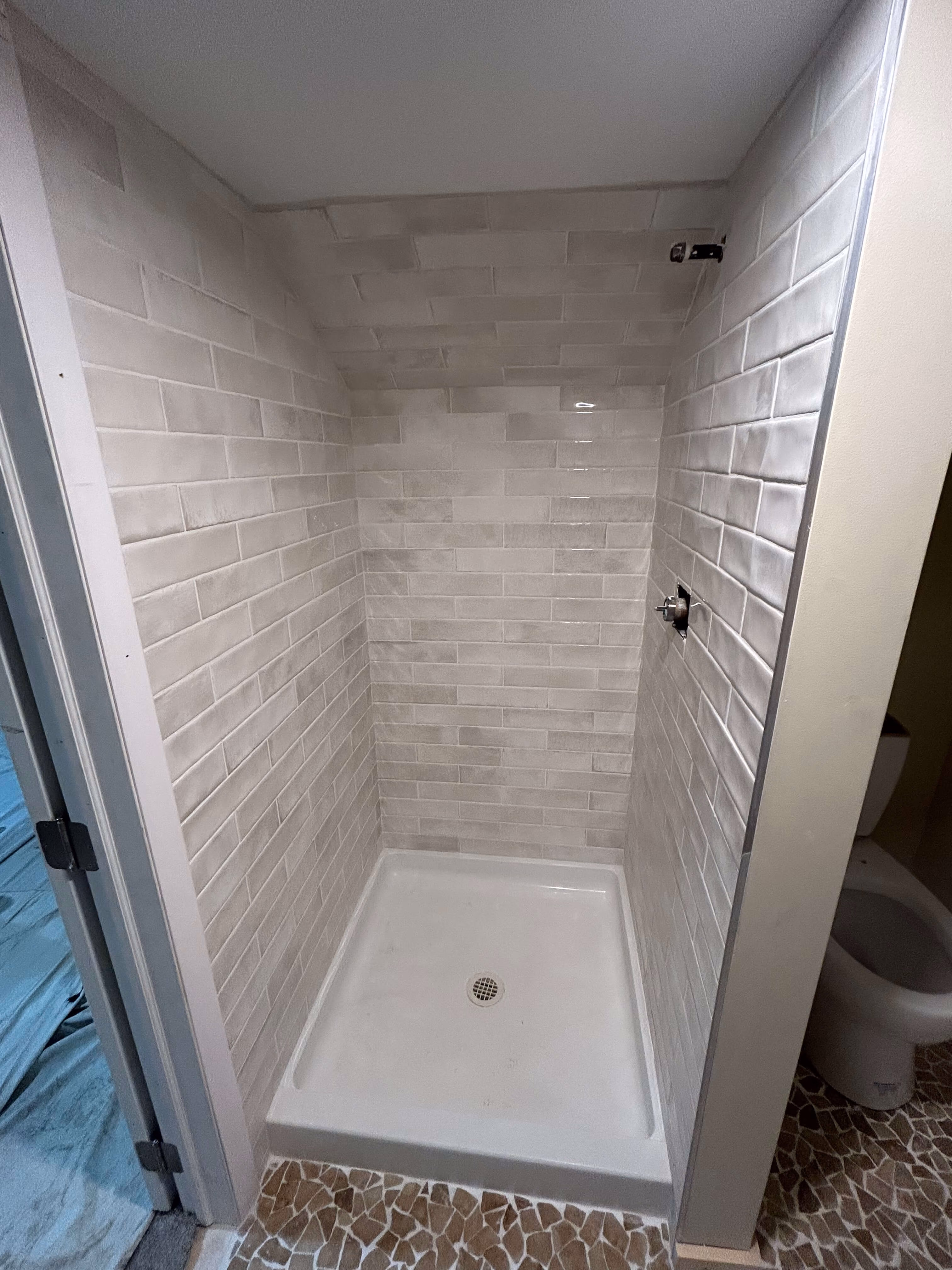 Empty tiled shower stall with white base and beige brick-patterned wall tiles in a bathroom.