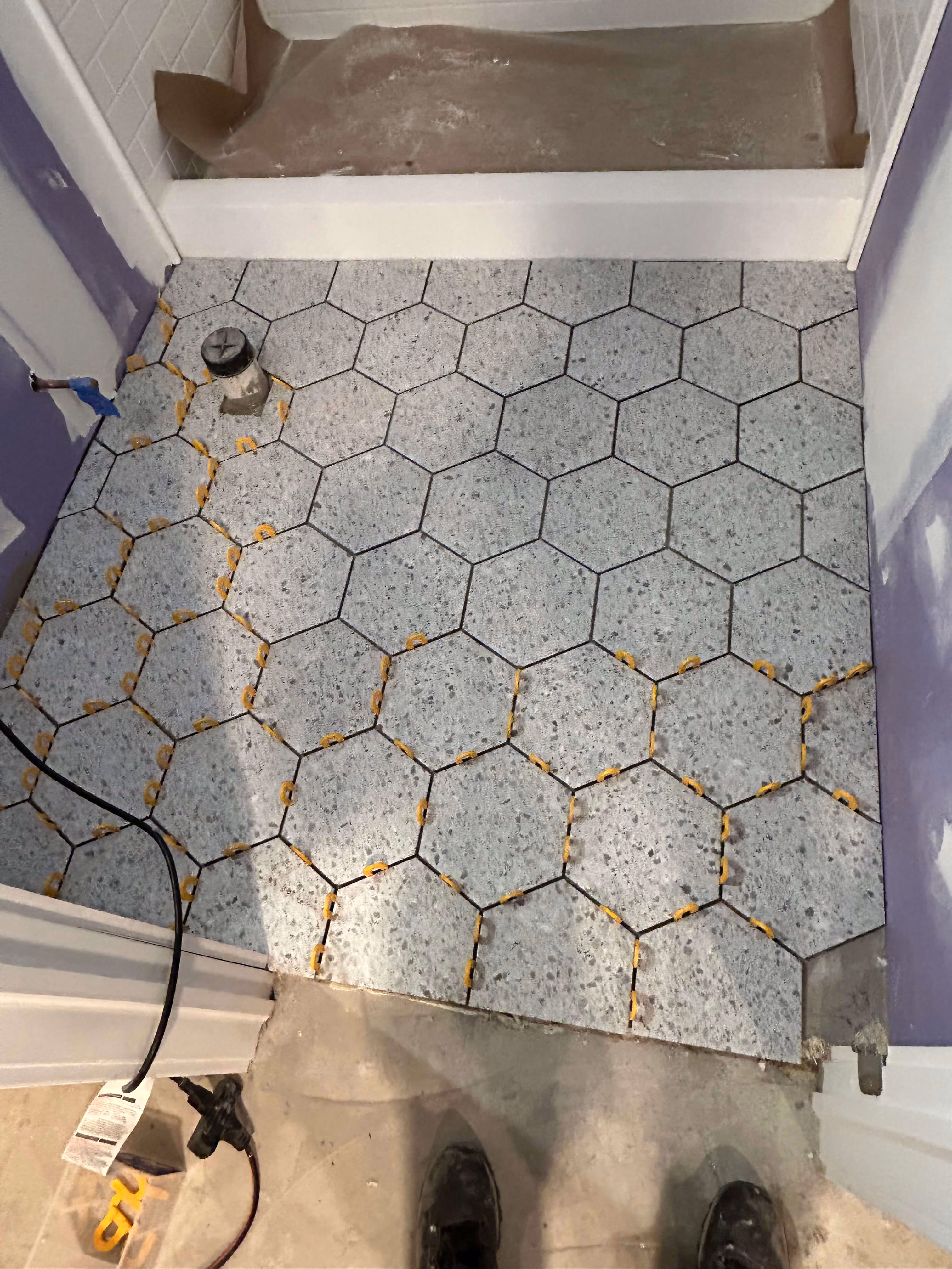 Hexagonal gray floor tiles being installed in a small room with tile spacers between edges.