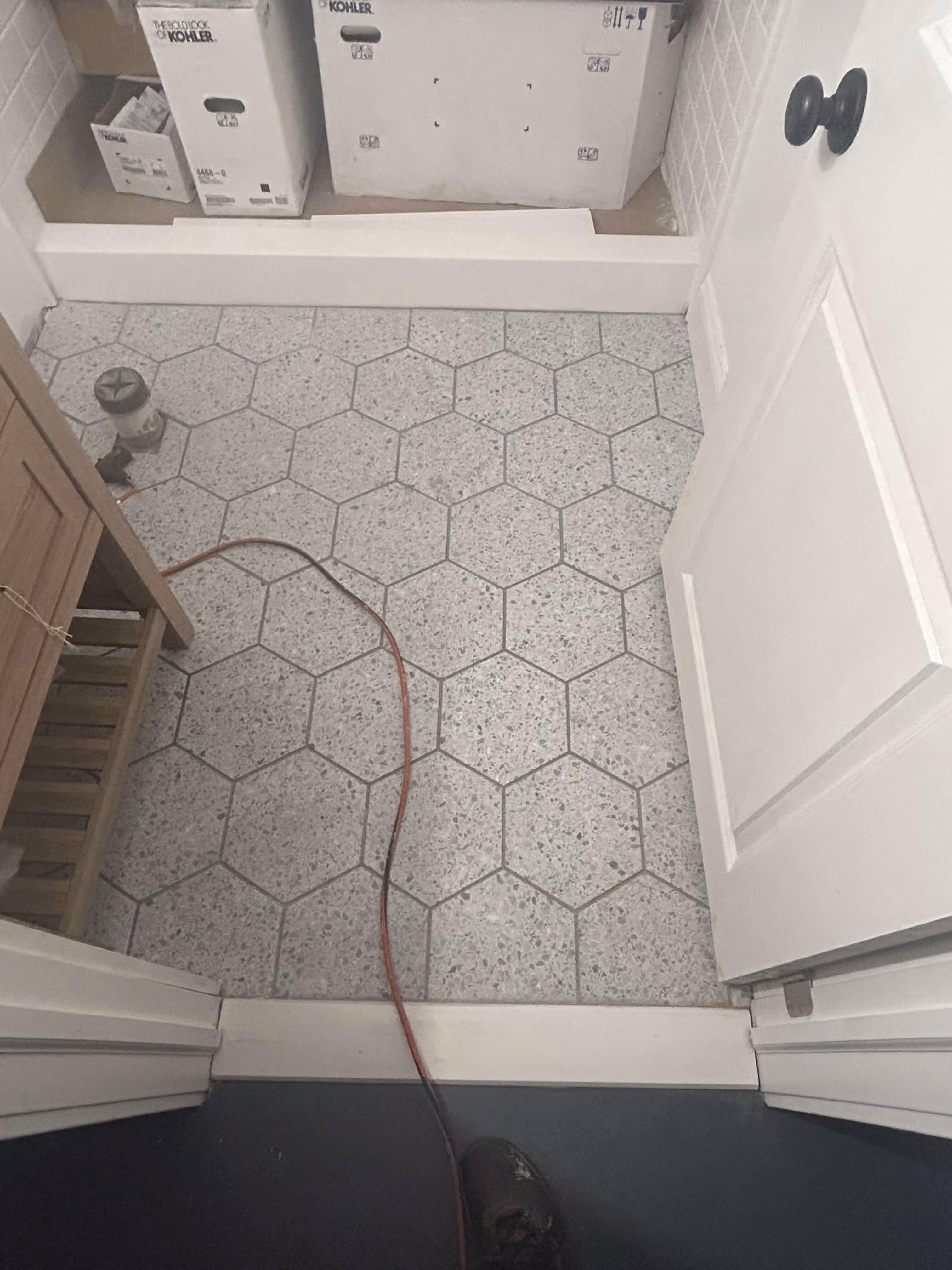 Hexagonal gray floor tiles in a small room with white door, wooden cabinet, and boxes on a shelf.