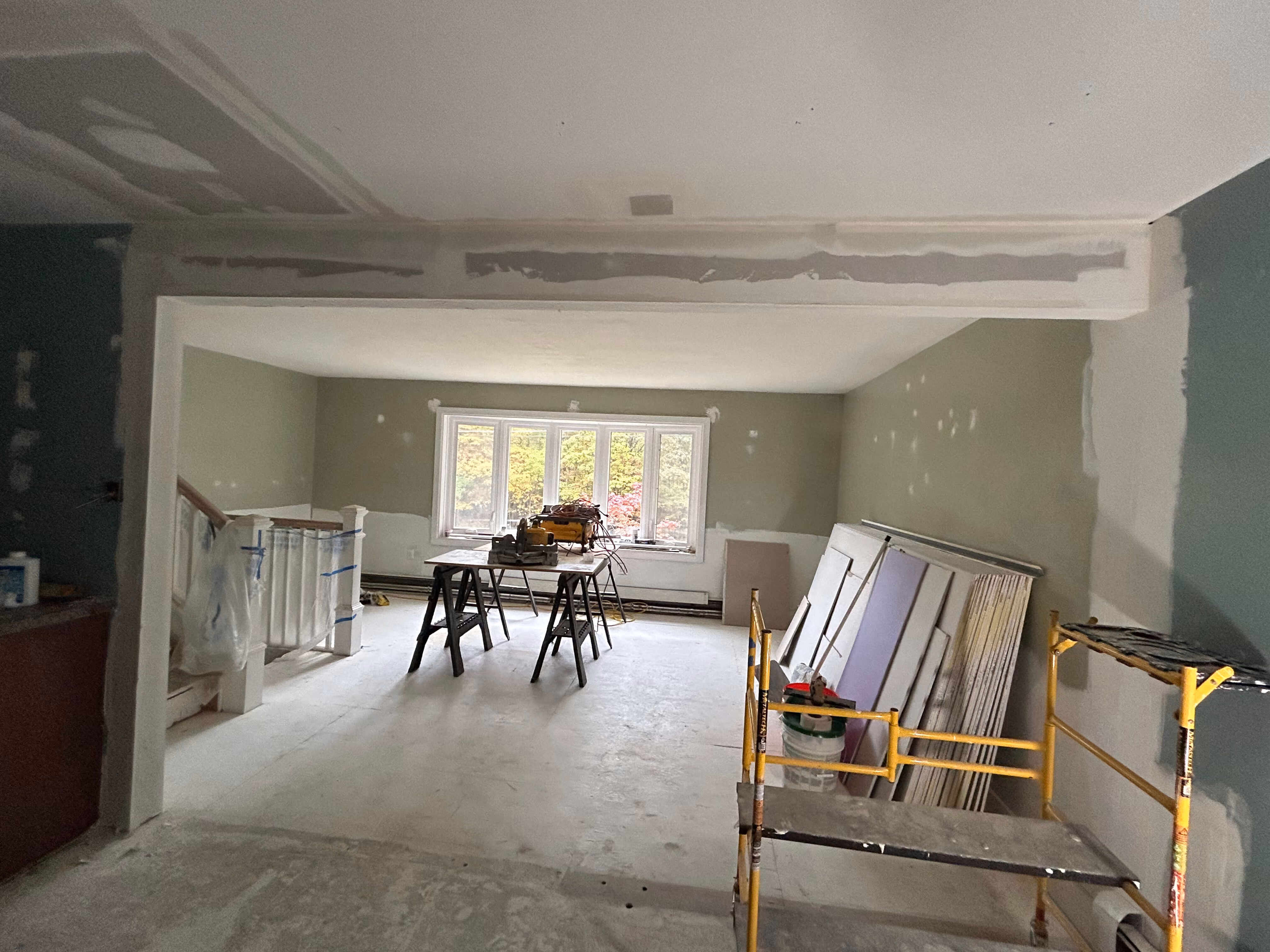 Room under renovation with unfinished walls, window at back, construction table, and scaffolding.