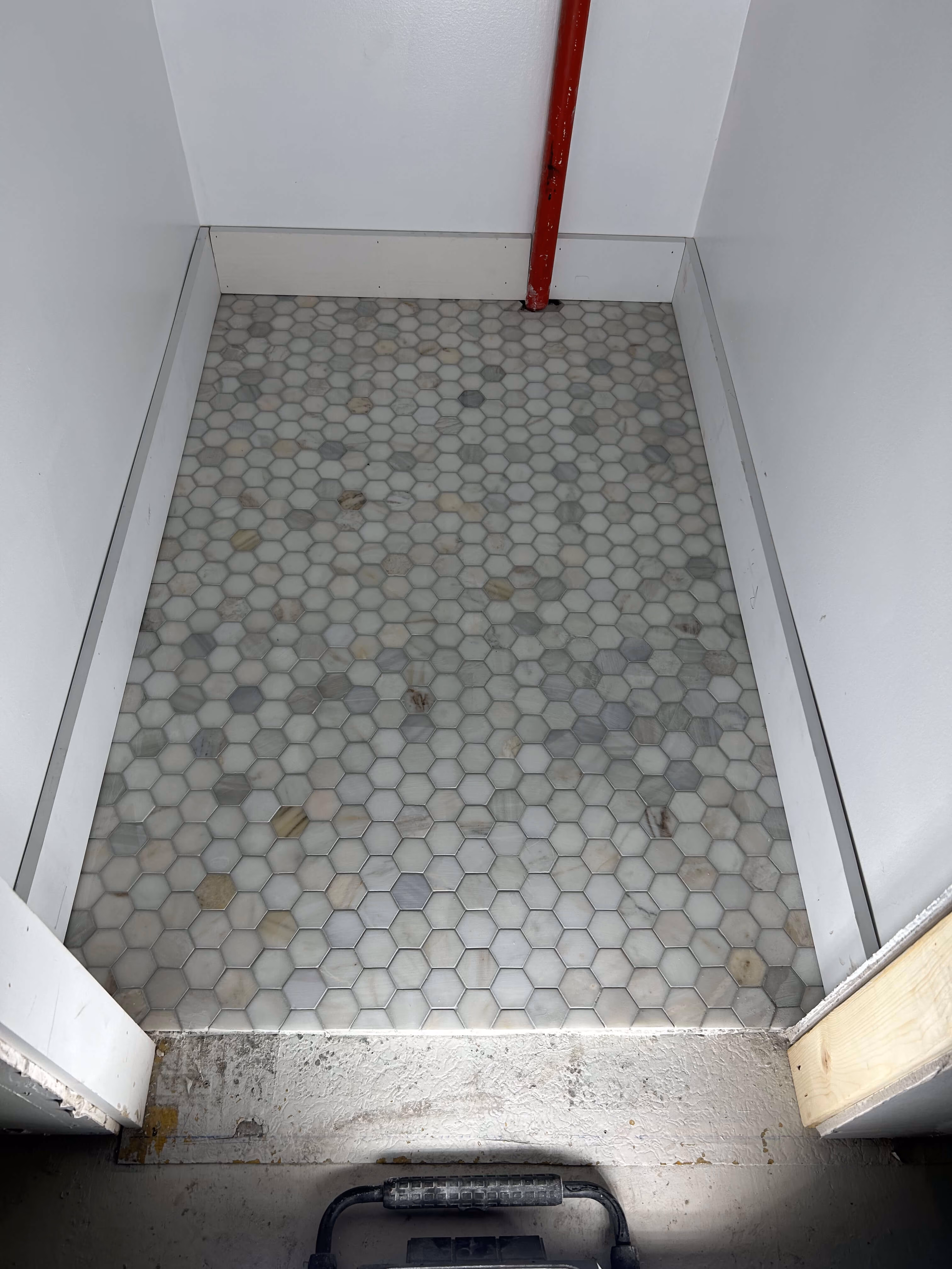 Floor with hexagonal mosaic tiles in gray and beige tones inside a small white-walled space.