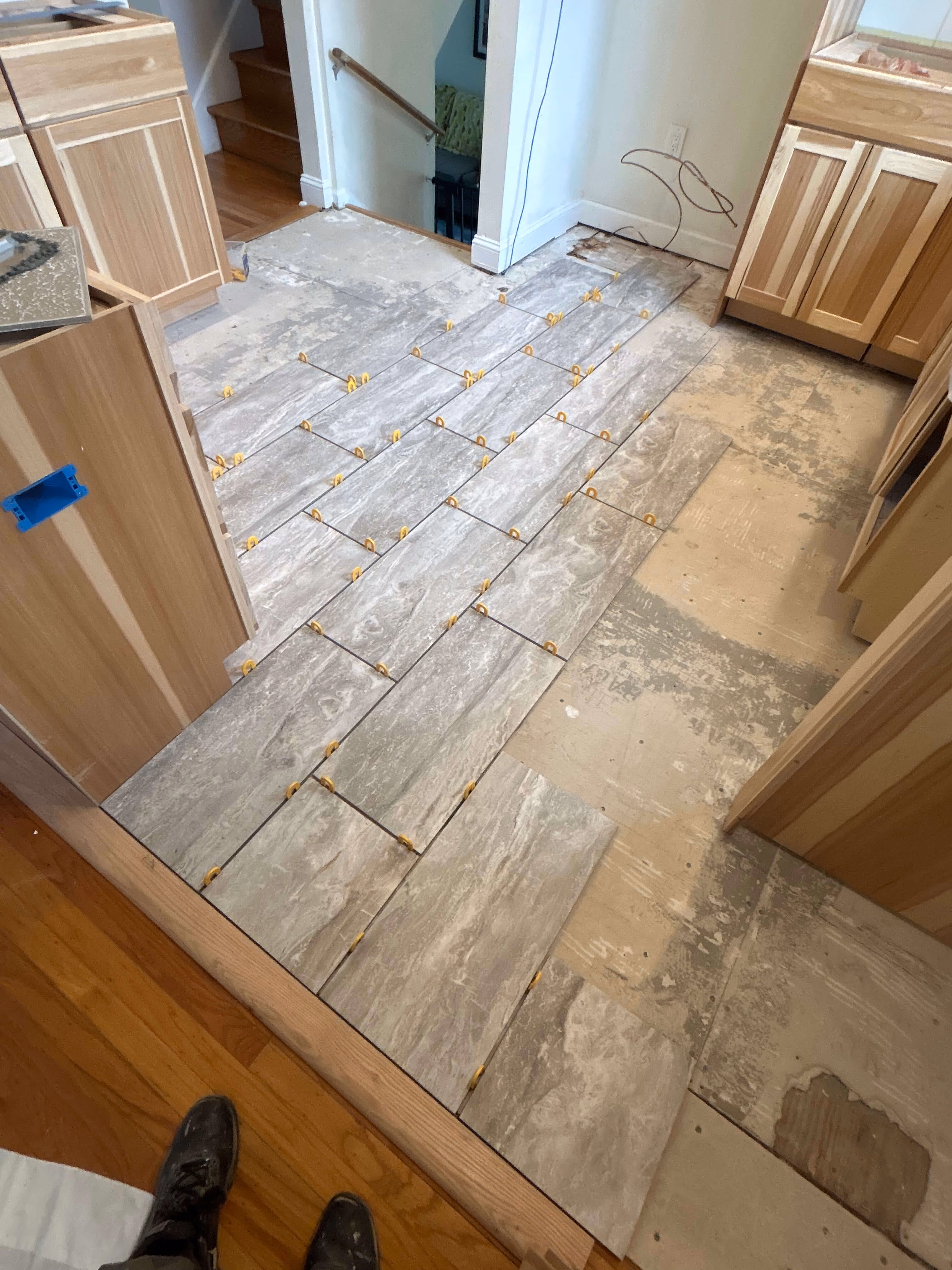 Partially tiled kitchen floor with gray rectangular tiles being installed using yellow spacers.