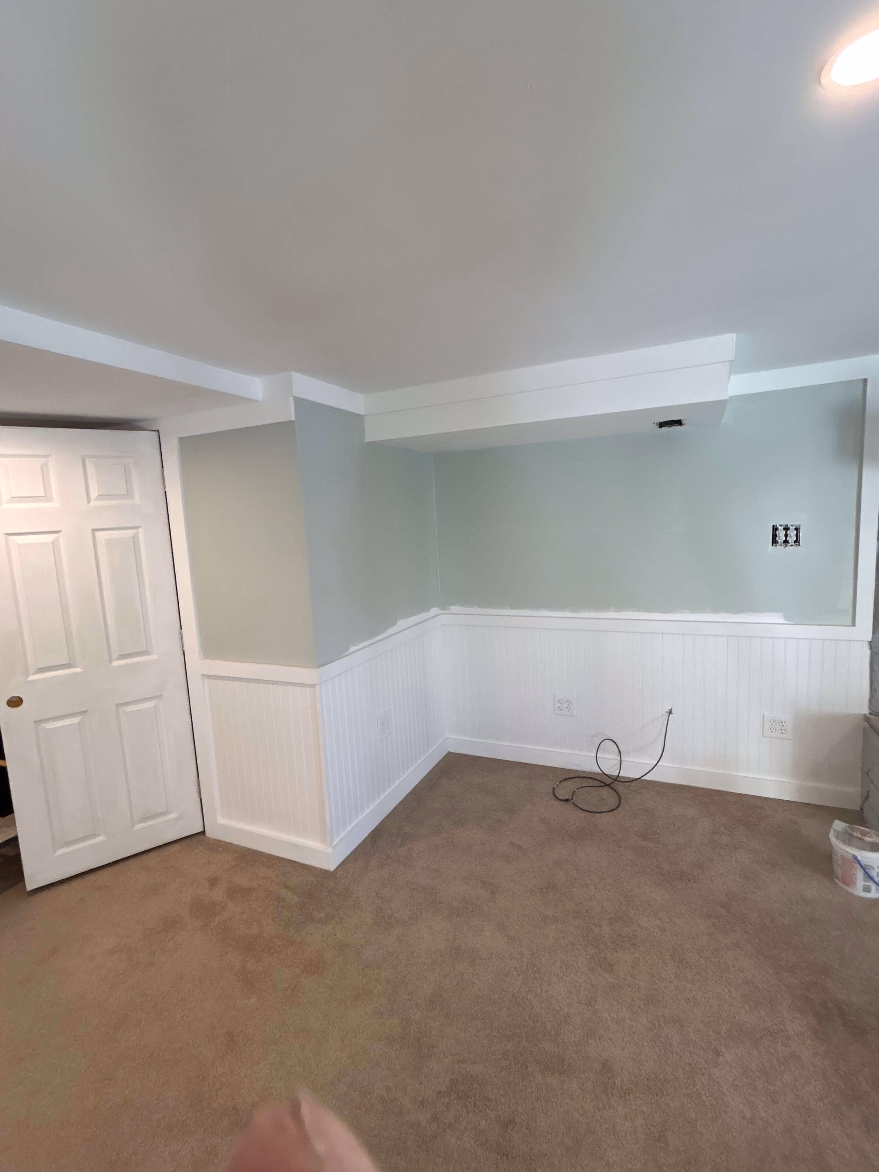 Empty room with beige carpet, light green walls, white wainscoting, and an open door on the left.