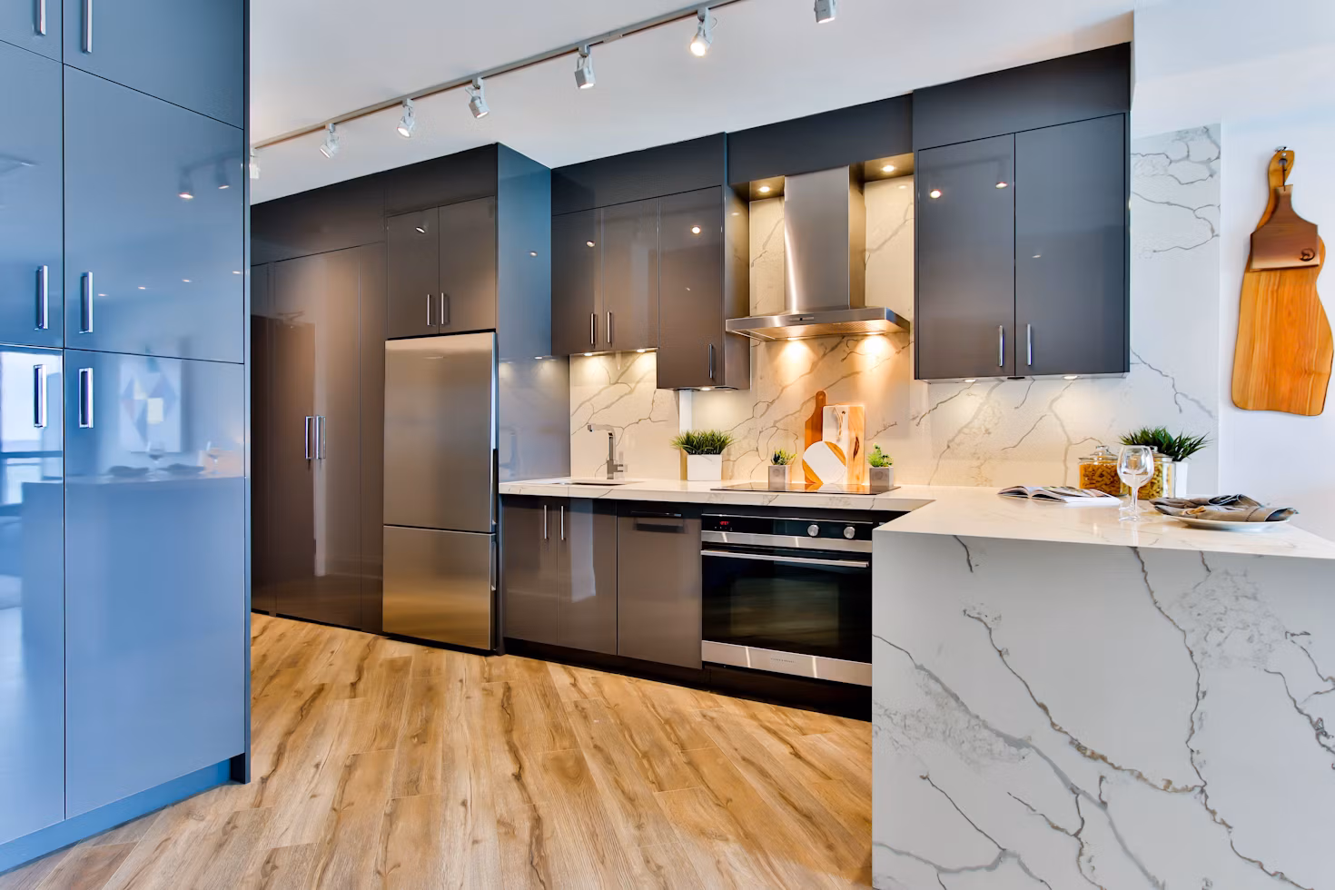 Modern kitchen with sleek gray cabinets, stainless steel appliances, marble countertops, and wooden floor.