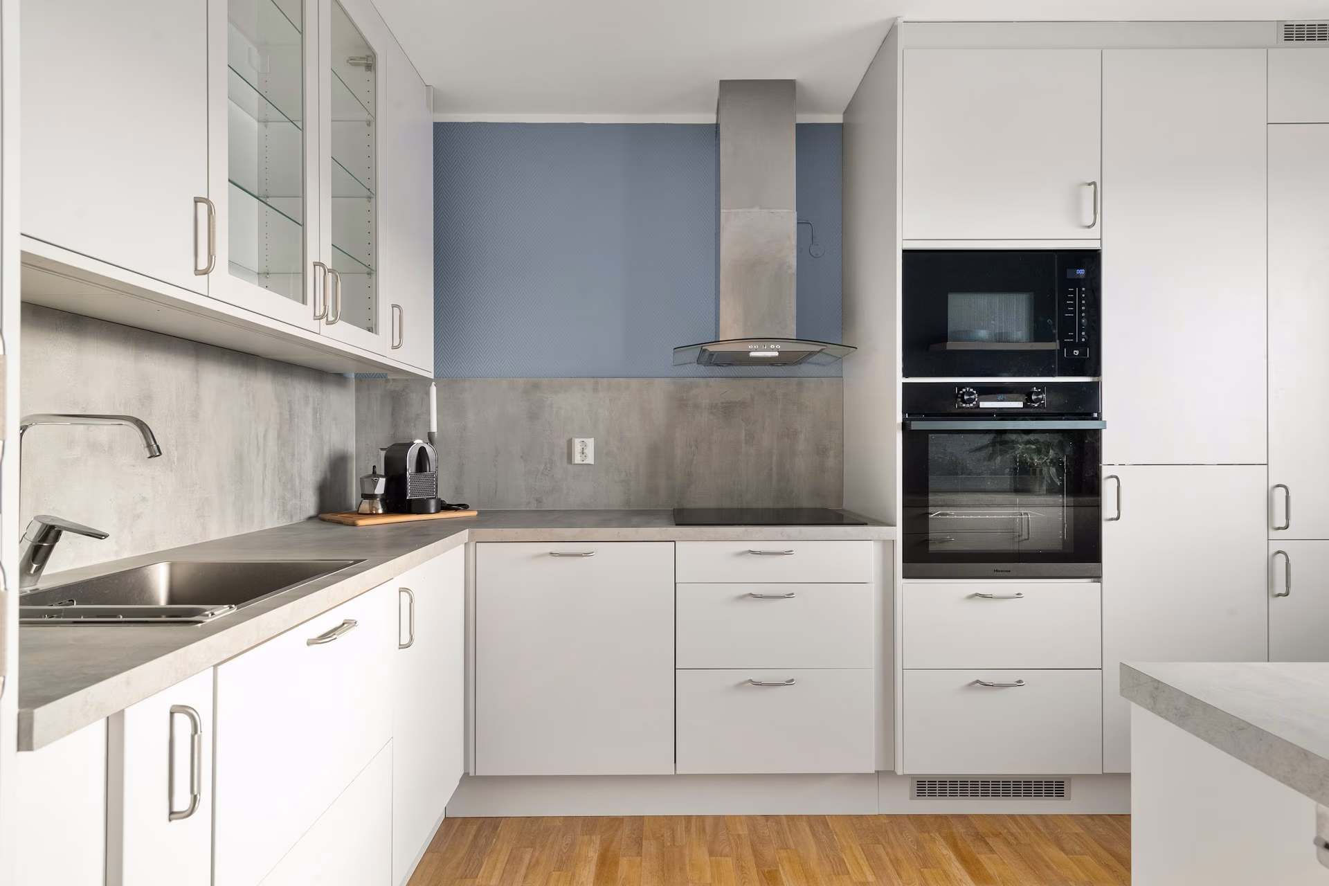 Modern white kitchen with built-in oven, stovetop, range hood, and wood flooring.